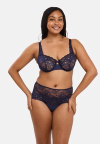 Navyblauwe kanten bh en hooggesneden slipset met ingewikkelde bloemmotieven en een gladde onderlaag. Beveiligd met verstelbare bandjes.