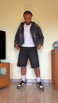 JAQUETA DE ESPORTIVA CINZA sobre uma t-shirt branca, combinada com calções de ganga pretos e ténis pretos. Os acessórios incluem meias brancas com logótipos.