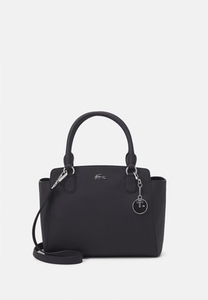 Bolso estructurado negro con dos asas, correa de hombro desmontable, pequeño logo plateado de cocodrilo y colgante redondo plateado para llavero.