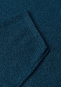 Gros plan d'un tissu tricoté bleu sarcelle plié montrant la texture et les détails du tissage.