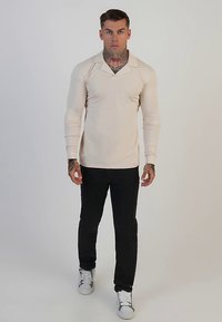 Cream long-sleeve polo with a pointed collar, fitted design, paired with black pants and white sneakers. Smooth fabric and minimal accents.