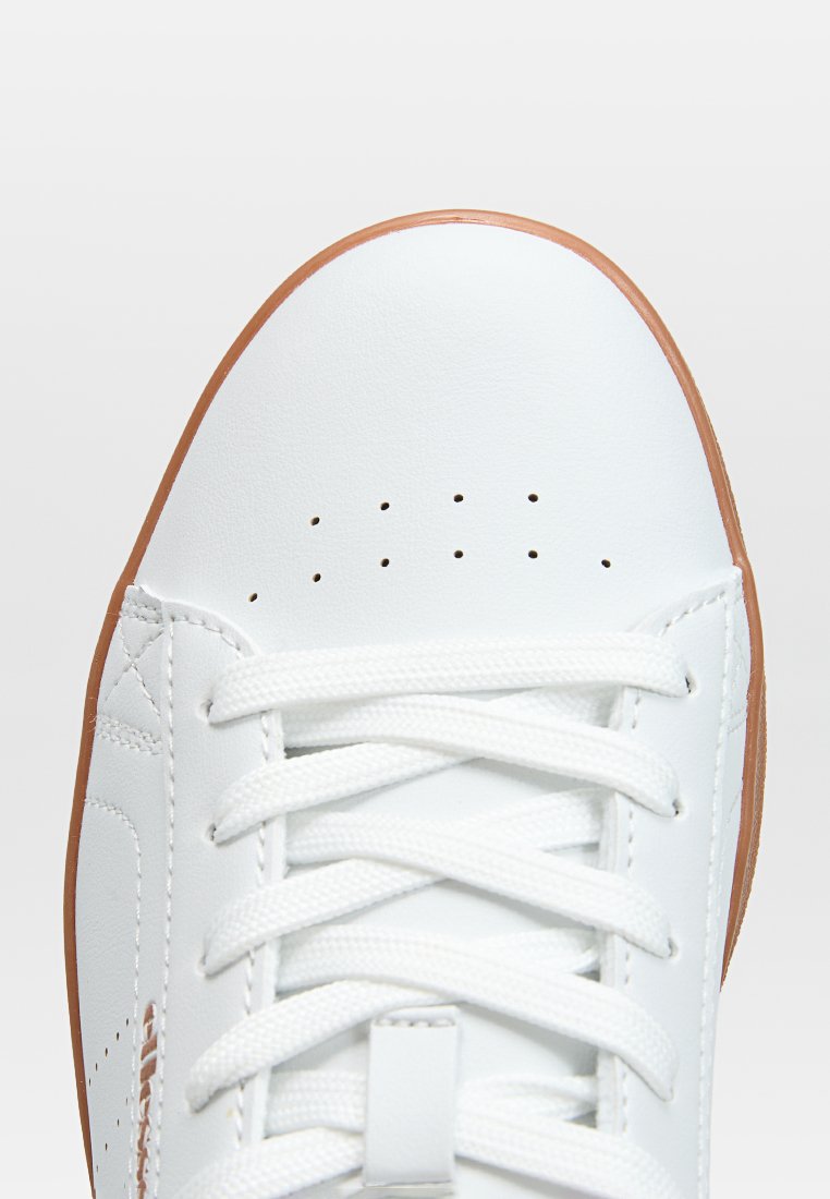 Zapatilla de cuero blanca con superficie lisa, puntera perforada, cordones blancos planos y suela de goma. Presenta un diseño minimalista y detalles de costura.