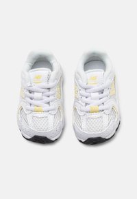 Baltos New Balance bėgimo bateliai su geltonais akcentais, tinkline šonine dalimi, paminkštintu kraštu ir juodu padu. Su raišteliais ir logotipu.