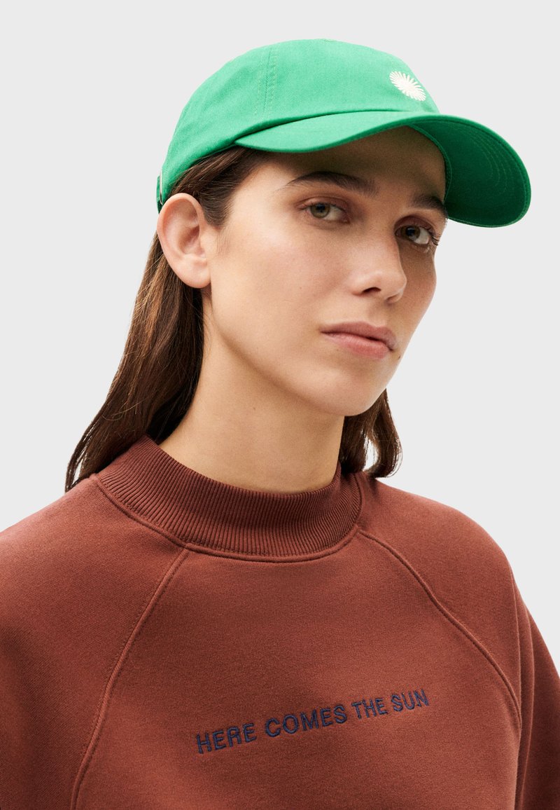 Casquette verte avec un logo à l'avant et un sweat-shirt marron comportant un texte brodé. Tissu lisse avec des couleurs contrastantes et un col côtelé.