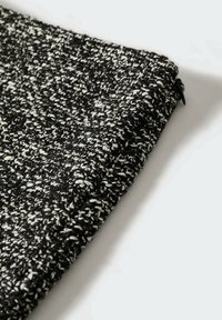 Tissu tricoté en noir et blanc avec un motif texturé et tacheté. Le morceau est plié et présente un bord net.