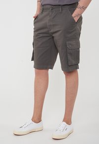 Pantaloni cargo color khaki realizzati in cotone, con tasche laterali, un fit rilassato e chiusura con bottone. Indossati con sneakers bianche.