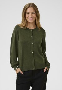 Zaļa kardigāna jaka ar mīkstu tekstūru, ar apaļu kakla izgriezumu un spīdīgām pogām gar priekšpusi. Garas piedurknes un brīvs piegriezums.