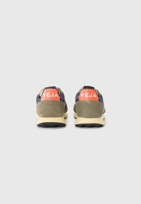Grønne og marineblå sneakers i ruskinnmateriale med en fremtredende rød VEJA-logo på hælen. Kremsfarget såle med teksturert svart yttersåle.