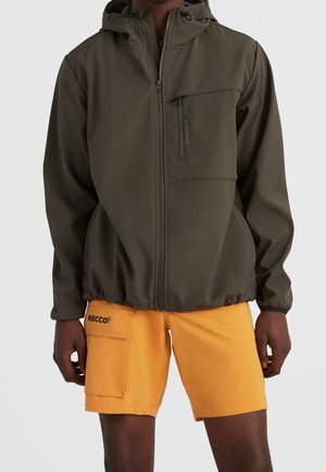 Mand iført olivengrøn hættetrøje med lynlås og lyseorange shorts med sidelomme og RECCO-logo på venstre lår.