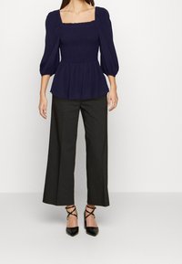 Top peplum blu con scollatura quadrata e maniche a sbuffo, abbinato a pantaloni neri a gamba larga a vita alta e decolletè neri a punta.