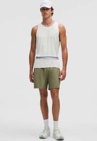 Top atlético sin mangas blanco, pantalones cortos verde oliva, cinturón morado claro, zapatillas blancas y gorra blanca; tejido suave y ligero.