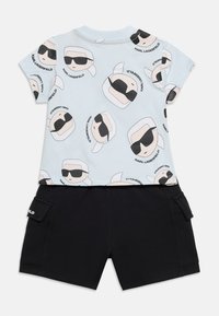 Costum pentru copii cu tricou albastru deschis, având fețe de desene animate cu ochelari de soare și pantaloni scurți negri cu buzunare laterale.