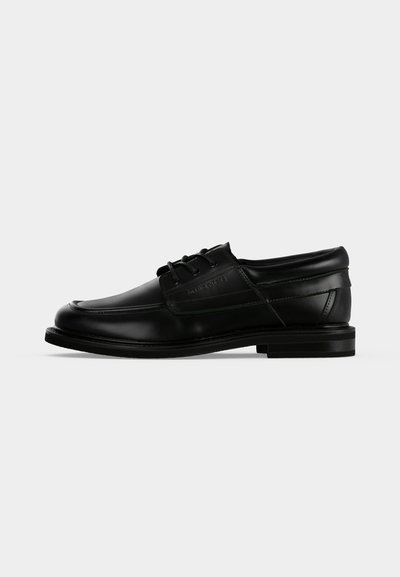Chaussure habillée pour homme en cuir noir avec lacets, talon bas et nom de marque embossé sur le côté, vue de profil sur fond blanc.