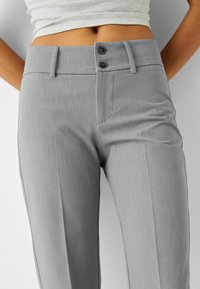 Graue, maßgeschneiderte Hosen mit glatter Textur, flacher Vorderseite, zwei Knöpfen am Bund und seitlichen Taschen.