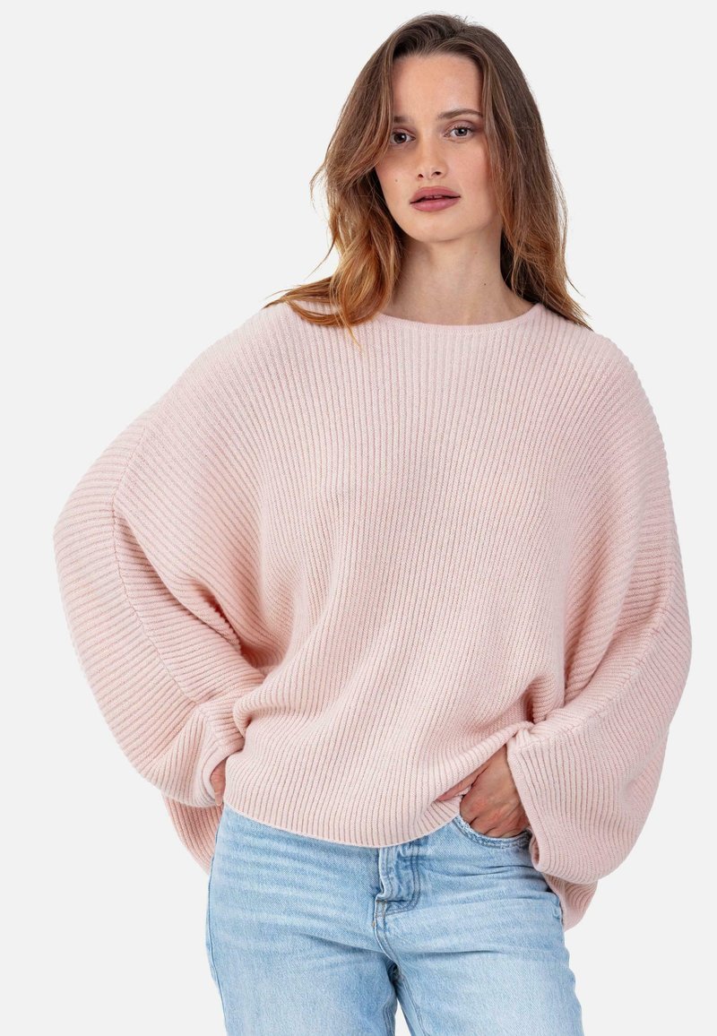 Pull en maille côtelée rose clair avec une coupe ample et large manches, associé à un jean bleu clair. Texture douce, design simple.