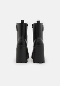 Bottines plates-formes noires en faux cuir lisse. Comprend un talon épais empilé, des fermetures éclair à l'arrière et des languettes de traction à l'arrière.