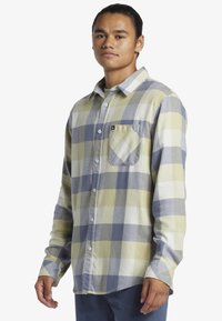 Langemouwen geruite shirt met een gele, blauwe en witte ruitpatroon; knoopsluiting; enkele borstzak; zachte stoftextuur.