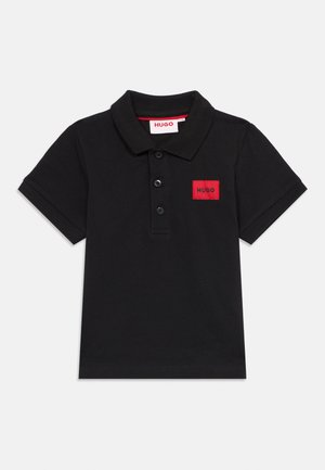 Sort kortermet poloshirt med tre knapper og et rødt rektangulært merke med påskriften "HUGO" på venstre bryst.