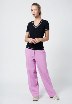 Top nero in maglia con bordi a scallop e scollatura a V, abbinato a pantaloni a vita alta di un rosa chiaro e sneakers argento. Design liscio e aderente.