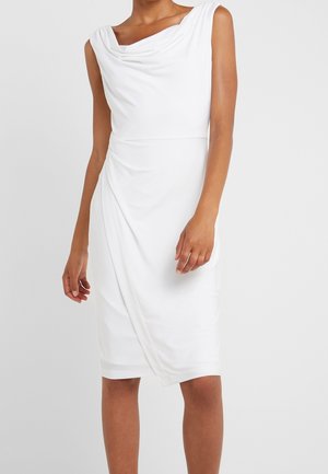 Woman wearing a sleeveless white knee-length dress with a draped neckline and gathered asymmetrical front detail.