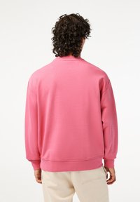 Sweat-shirt à col ras du cou de couleur rose vif, confectionné en tissu doux. Il présente un col rond, des manches longues et des poignets en côte. Design minimaliste.