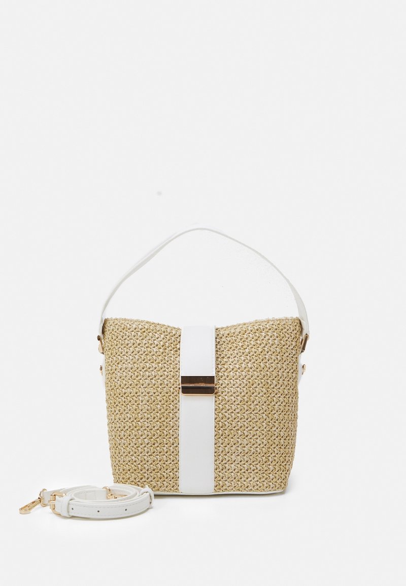 Geflochtene Strohtasche mit weißem Lederhenkel und vertikalem weißen Lederdetail, das durch eine goldene Schnalle gesichert ist, daneben ein abnehmbarer weißer Schultergurt.