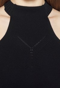 Černý pletený halter top s vysokým výstřihem, texturovanou tkaninou a trojúhelníkovým otevřeným vzorem uprostřed. Hladké okraje.