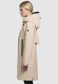 Beige waterdichte regenjas met een capuchon, zijzak met rits en drukknoopmanchetten; gladde textuur en eenvoudig ontwerp.