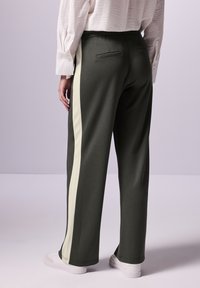Mörkgröna sweatpants med vita sidostreck, med en avslappnad passform, elastisk midja och två bakfickor. Bärs med vita sneakers.