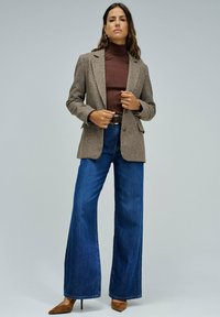 Blazer marrón a cuadros, suéter de cuello alto marrón, jeans de campana de cintura alta azules y tacones de punta marrón. Texturas suaves, diseño ajustado.