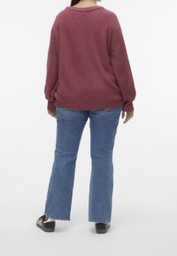 Pull en maille bordeaux avec un motif texturé, manches larges et ourlet côtelé, associé à un jean évasé bleu clair et des baskets noires.