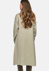 Lange olijfgroene jas gemaakt van zachte, gestructureerde stof. Heeft een ontspannen pasvorm en verlaagde schouders, die tot halverwege de kuit reikt.