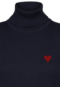 Tumesin turtlenecki sviiter, valmistatud ribakujulisest materjalist, millel on vasakul küljel väike punane tikitud süda. Pehme tekstuur ja lähedalt istuv disain.