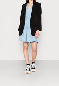 Mustapuku vaaleansinisen kerroksittaisen mekon päällä, jossa on V-pääntie. Musta-valkoiset lenkkarit täydentävät asun.