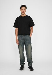 Black cotton t-shirt paired with blue denim cargo pants featuring patchwork details, and black sneakers. Simple design with a relaxed fit.