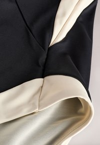 Gros plan sur un tissu noir et beige avec des détails de couture et une doublure en mesh à l'intérieur, montrant la texture et la construction d'une manche de vêtement.