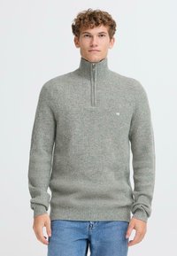 Maglione grigio a maglia con colletto alto e design a mezza zip. Presenta una texture a coste e un piccolo logo sul petto. Vestibilità casual.