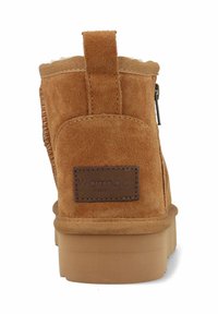 Bruine suède enkellaars met een gladde textuur, gebogen vorm, een trekhaak aan de achterkant en een tan rubberen zool. Logo patch op de achterkant.