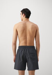 Pantaloni da bagno grigio scuro con vita elastica, dotati di una singola tasca sul retro e realizzati in un tessuto leggero e strutturato.