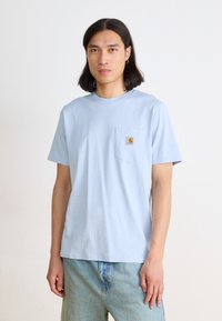 Light blue cotton t-shirt with short sleeves, round neckline, and a chest pocket featuring a small logo patch. Casual fit.