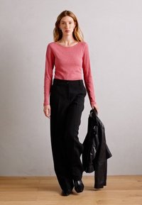 Ilgām piedurknēm rozā džemperis ar apaļu kakla izgriezumu, apvienots ar augstu jostasvietu melnām biksēm. Tur rokās melnu ādas jaku. Gluda tekstūra.