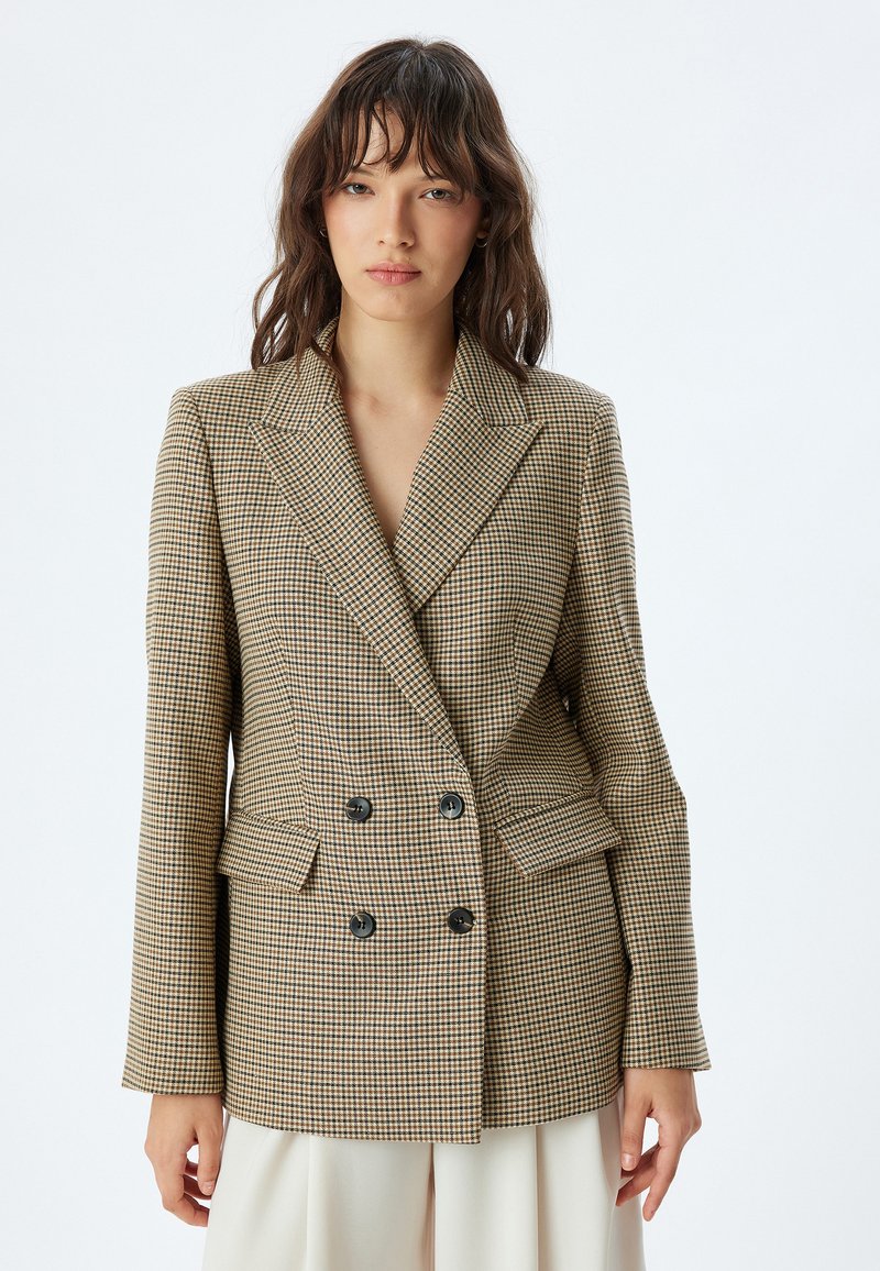 Blazer doppiopetto con motivo a quadri in beige e marrone. Presenta un colletto a revers, due tasche frontali e bottoni neri.