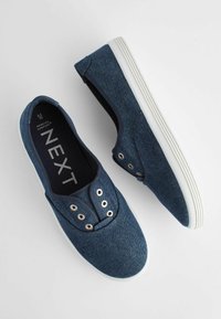 Blå denim slip-on sko med hvide gummisåler, der har fem metaløjer, rund tå og elastiske sideaccenter for nem påtagning.