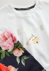 Biele bavlnené tričko s potlačou zlatého textu „BAKER“, dekoratívnymi motívmi kľúča a srdcovej zámky a kvetinovým vzorom na rukáve.