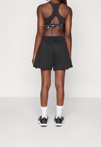 Černá sportovní podprsenka s designem racerback a páskem s logem, doplněná volnými černými šortkami. Bílá ponožky a černé tenisky dokončují vzhled.