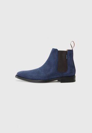 Bottine en suède bleu marine avec des panneaux latéraux élastiques, une languette, un bout rond et une semelle en caoutchouc noir. Texture lisse avec un minimum de détails.