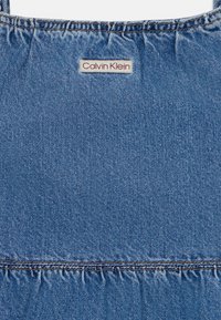 Jeans obleka z nabranim vrhom, ki ima znamko Calvin Klein. Svetlo modra barva, srednje teža, z gladko teksturo in enotnim vzorcem.