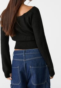 Zwarte gebreide trui met een brede ronde halslijn, ribbelzoom en lange mouwen, gecombineerd met high-waisted blauwe denim cargobroek met achterzakken.