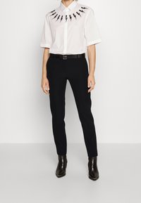 Vit kortärmad skjorta med svart blixtdesign runt kragen, kombinerad med svarta slim-fit byxor och spetsiga svarta ankelboots.