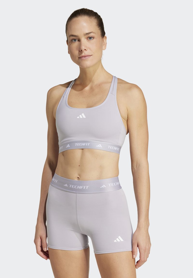 Lichtpaarse sport-bralette met logo en bijpassende high-waisted shorts, gemaakt van rekbare stof; gladde textuur en minimalistisch ontwerp.